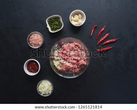 Minced meat and a set of ingredients for cooking on a black table.