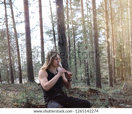 A musician with a tool in nature. Man is playing a flute in a pine forest. The music of the druids in the spring forest.
