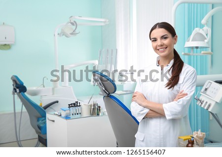Young female dentist in white coat at workplace. Space for text Royalty-Free Stock Photo #1265156407