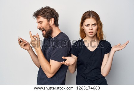 A cheerful man is looking at the phone and the perplexed woman next to him spreads his hands            