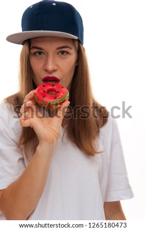 A caucasian woman in blue hip hop loose her hair down wearing cap opens mouth to bites a delicious yellow donut in her hand