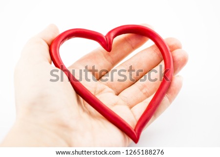Closeup of girl's hand. She holds a plastic heart frame. The background is white