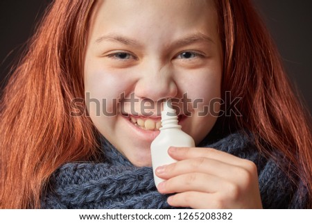 Sick girl with warm scarf around her neck is holding bubble in her hand with drop from runny nose near her nose
