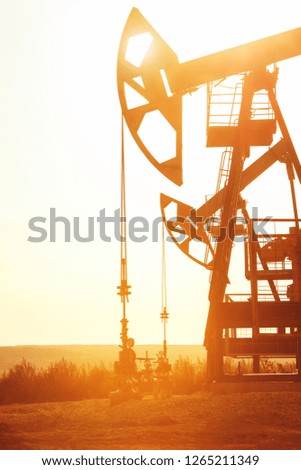 Pumping unit is working in oil field on the sunset background