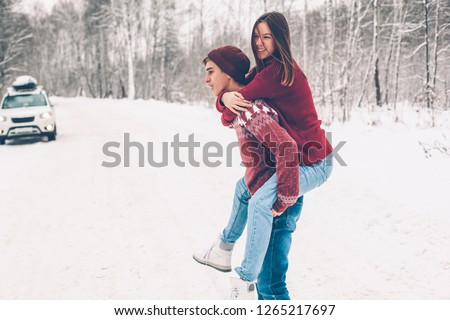 Photo of teenage friends in red Christmas sweaters playing in snow one winter day. People having road trip on the January weekends.