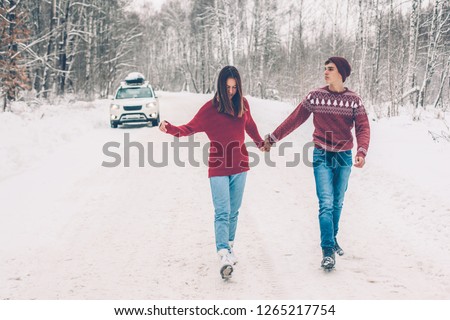Photo of teenage friends in red Christmas sweaters walking in snow one winter day. People having road trip on the January weekends.