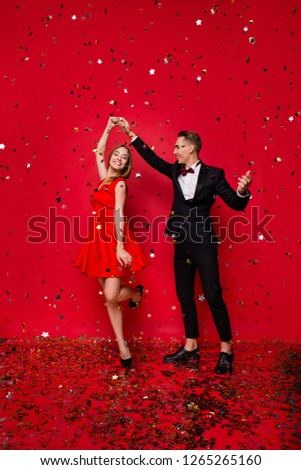 Vertical full length body size view of two exquisite gorgeous attractive positive married spouses rejoicing among flying decorative elements having fun isolated on bright vivid shine red background