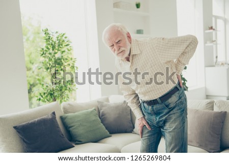 Close up photo of grey haired he his him granddad alone in big house can not find phone to call emergency wearing casual checkered shirt jeans denim outfit in front of cozy divan
