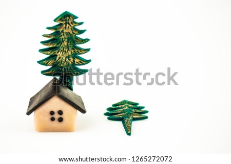 Left close up on a white background is a small toy house and a tree, next to it is a small tree. Copyspace