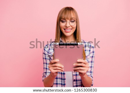 Portrait of nice cute adorable attractive winsome cheerful straight-haired girl in checked shirt holding in hands reading e-book isolated over pink pastel background
