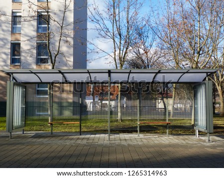 bus shelter at a bus stop of glass and aluminum structure in park-like setting with green background and appealing safety glass design with benches. poster billboard display glass. transparent look