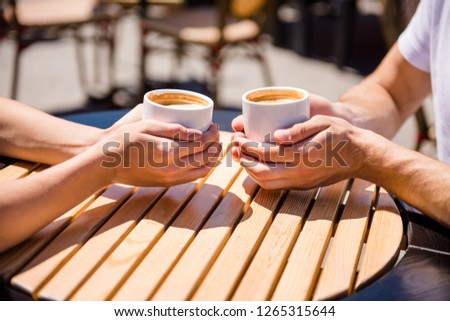 Cropped close-up view of two nice pair of hands holding cups hot chocolate married spouses husband wife spending honey moon outside in park