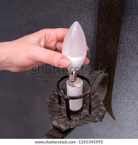 A woman's hand inserts an led light bulb into the wall lamp. Royalty-Free Stock Photo #1265345995