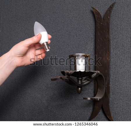 A woman's hand inserts an led light bulb into the wall lamp. Royalty-Free Stock Photo #1265346046
