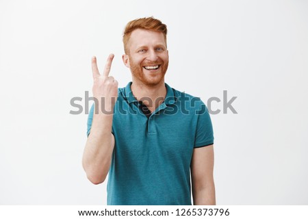 Showing you two steps to successful business. Portrait of friendly-looking happy and joyful redhead male with beard making sign twice and smiling broadly while standing over gray background