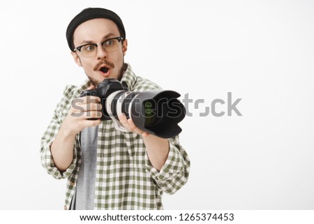 Waist-up shot of impressed and excited cute male photographer working on new project holding camera opening mouth in wow sound staring thrilled and amused right seeing awesome idea for picture
