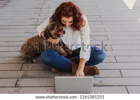 beautiful young woman having fun with her cute brown dog and working on laptop. Indoors