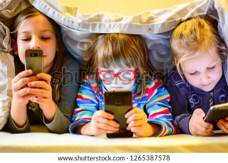 Children play games on a smartphone at mourning under a blanket on the bed. The child's face is illuminated by a bright monitor. Staying at home can help stop coronavirus spreading concept. Royalty-Free Stock Photo #1265387578
