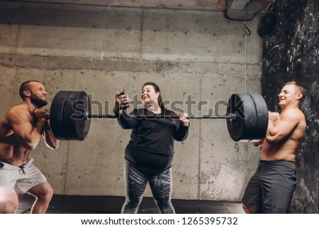 crazy fat girl taking a picture of herself while sportsmen lifting the barbell. close up photo. fun