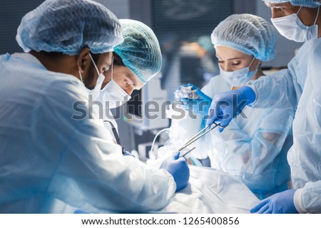 Concentrated Surgical team operating a patient in an operation theater. Well-trained anesthesiologist with years of training with complex machines follows the patient throughout the surgery. Royalty-Free Stock Photo #1265400856