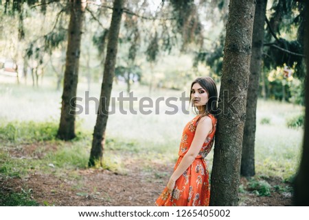 Beautiful young girl in a summer red dress in a park.