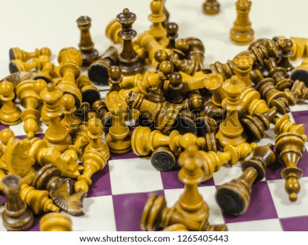 Beautiful and diverse subject. Beautiful wooden lacquered chess pieces scattered chaotically and randomly on a chessboard at close range in a dark interior.