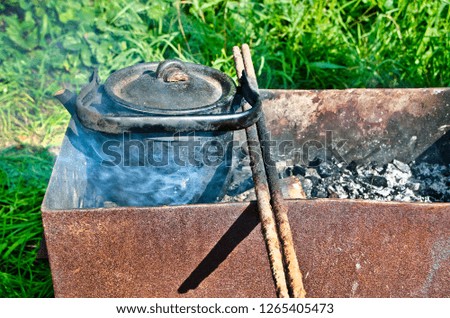 Beautiful and diverse subject. An old and dilapidated black kettle in the soot, on the fire of a fire and on a makeshift barbecue on the nature in the summer afternoon.