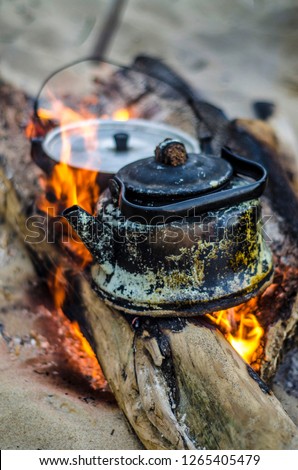 Beautiful and diverse subject. An old and dilapidated black kettle in the soot of a fire on the fire in nature in the summer afternoon.