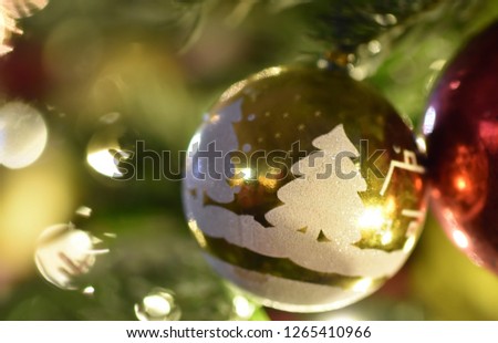 Golden Christmas ball with white pictures on a branch of a green holiday spruce with yellow bokeh and highlights