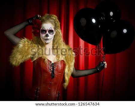 Portrait view of a female wearing sugar skull with black balloons over red background.