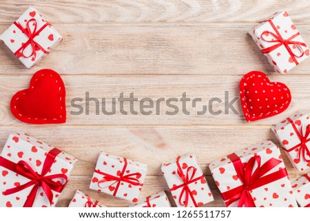 Valentine or other holiday handmade present in paper with red hearts and gifts box in holiday wrapper. Present box of gift on orange wooden table top view with copy space, empty space for design.
