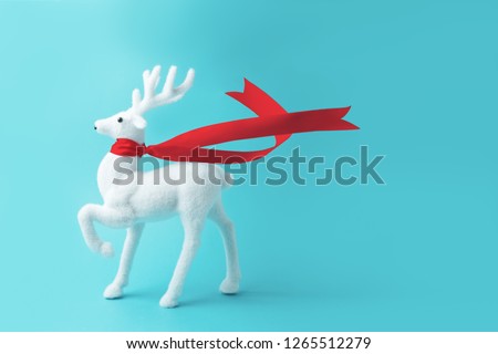 White reindeer with red ribbon on blue background. Christmas or New Year minimal concept.