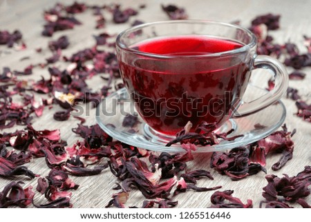 Hibiscus tea in a glass cup on a wooden table among the rose petals and dry tea. Vitamin tea for cold and flu.