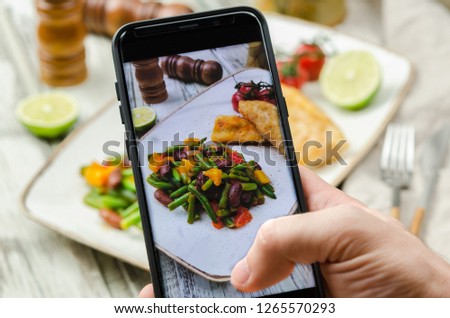 Young man taking photo of fish and vegetables plate on smartphone. Taking food photo with mobile phone.