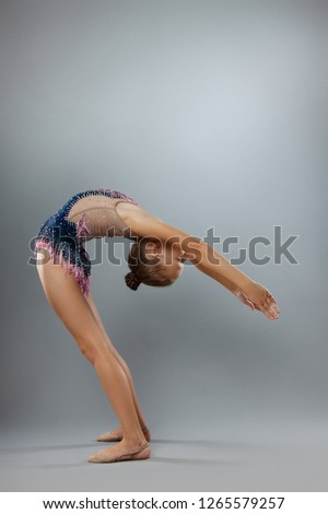 Beautiful flexible gymnast in sports outfit performs an element of rhythmic gymnastics on a gray background.
