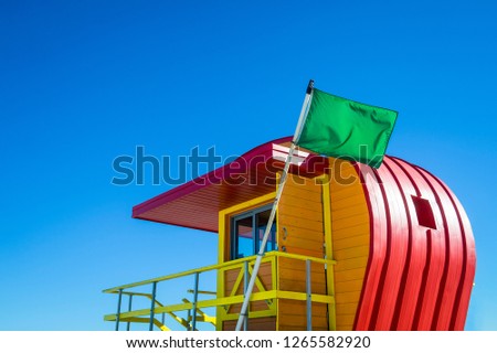 Bright scenic fine weather view of green flag flying on a lifeguard tower, signaling good swimming conditions on the beach, under sunny blue sky
