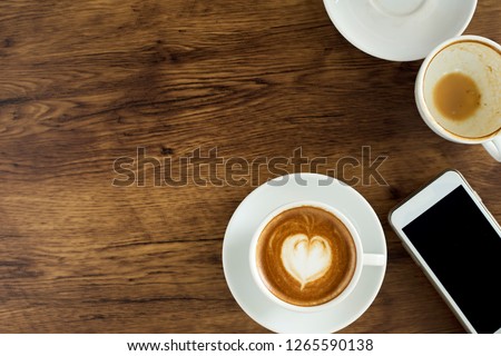 Cup of coffee with heart pattern in a white cup and smart phone on wooden background, Top view, Ideas for doing business online
