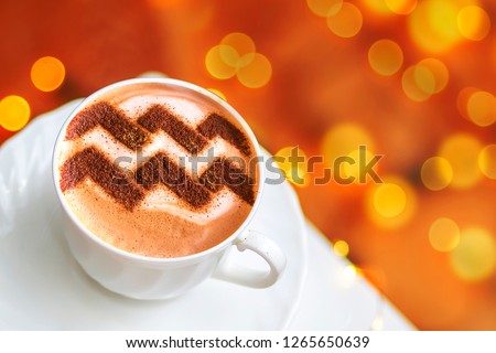 a cup of cappuccino coffee with a pattern of the aquarius aquarius zodiac sign on milk foam
