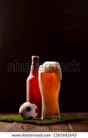Photo of buttle and glass of beer, soccer ball on green grass