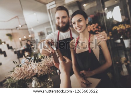 The girl pays to buy a bouquet of flowers florist. A young girl pays for the purchase of a bouquet of flowers by credit card. Bearded male florist accepts payment for a bouquet of flowers.