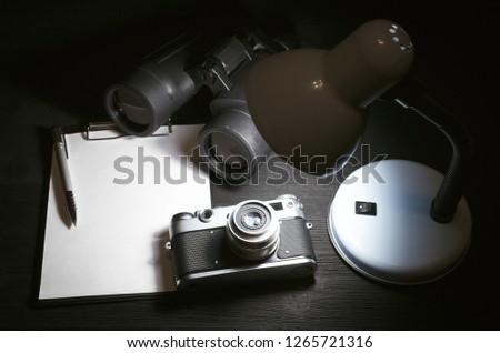 Blank page with copy space, pen, binoculars and photo camera on a black spy agent or paparazzi photograph table background. Interrogation. Surveillance concept.