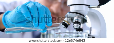 Male chemist holds test tube of glass in hand portrait overflows liquid solution potassium permanganate conducts an analysis reaction takes various versions of reagents using chemical manufacturing. Royalty-Free Stock Photo #1265746843