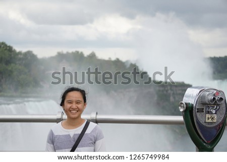 a asian tourist taking a picture on the observation tower of Niagara Falls, New York, overlooking the American falls; standing next to a coin operated binoculars 