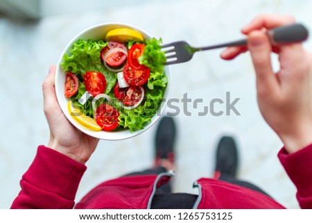 Young fitness woman in sneakers is eating a healthy, fresh salad after a workout. Fitness and healthy lifestyle concept. Top view  Royalty-Free Stock Photo #1265753125