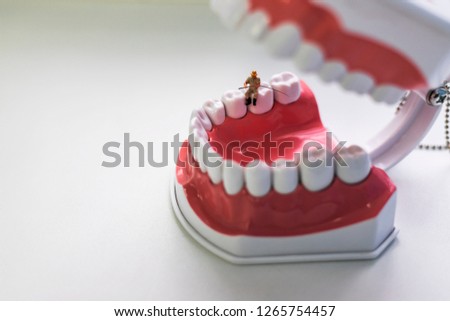 Miniature figures. Men help to treat teeth. An old man sits in his jaw and catches fish. Saver for a dental clinic. On light background.