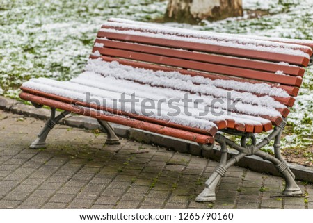 Isolated brown park bench  full of snow, and the Grass is also snow-covered. It´s Winter and it´s cold outside. Winter is coming in Avilés, Spain.