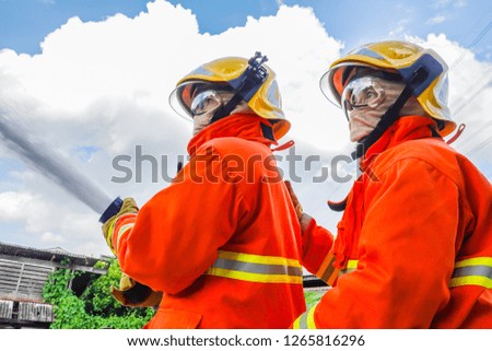 Two fireman trainning in fire fighting suit spraying water to fire surround on house background