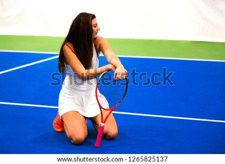 Young pretty female tennis player is smiling while sitting at the blue tennis court. Active lifestyle & sport concept