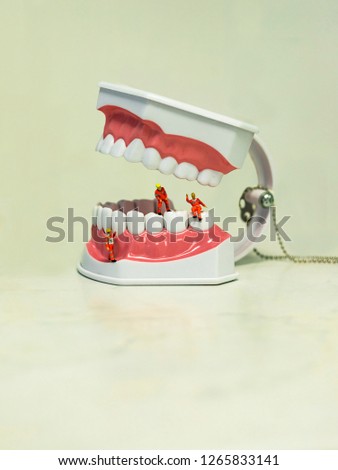 Miniature figures. Small workers are in a huge jaw with snow-white teeth.  Worker waving, the second examines the gums. The background for the dental clinic. On light background.