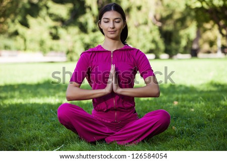 Beautiful young girl meditating while sitting on the grass in a park